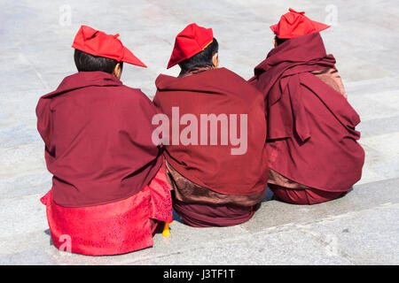 Trois jeunes moines bouddhistes Tibétains assis sur la chaussée à Lhassa au Tibet Banque D'Images