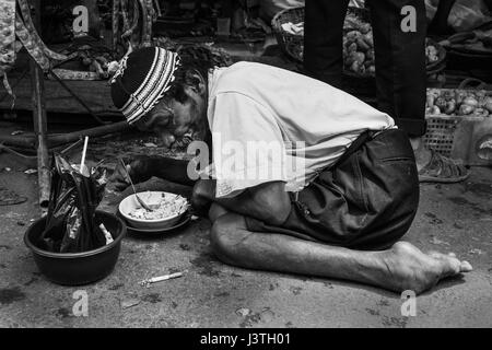 Portrait noir et blanc d'un pauvre vieil homme handicapé nouilles manger sur un terrain sur un marché à Sumatra Banque D'Images