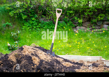 Une pelle dans un tas de sable et de terre dans un jardin au printemps Banque D'Images