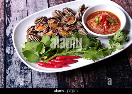 Frais et délicieux du sang à la coque coques surmontée du shell Red Chili, la coriandre et le céleri chinois servi avec sauce épicée en Corée noir motif di Banque D'Images