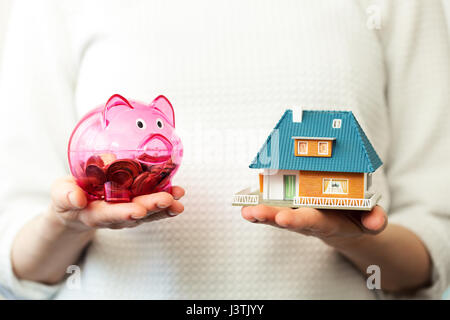 Économies pour nouvelle famille house concept - tirelire et maison modèle à l'échelle dans les mains Banque D'Images