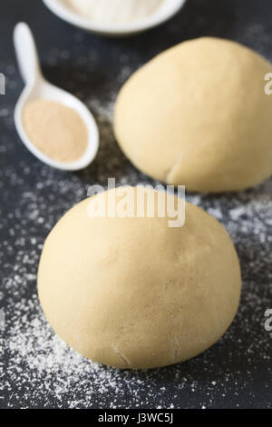 A augmenté ou boules de pâte de levure pour le pain ou la pizza sur une surface farinée, l'ardoise, les ingrédients à l'arrière, photographié avec un éclairage naturel Banque D'Images