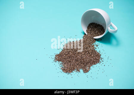 Les graines de chia nutritifs dans tasse sur fond bleu clair. Banque D'Images