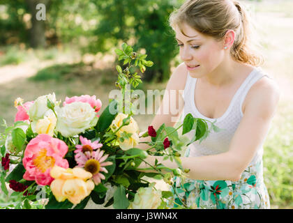 Bouquet, arrangement floral et concept - jeune femme en rose magnifique bouquet de pivoines, roses, œillets et les marguerites, fleuriste fille en robe blanche, en collaboration avec fleurs dans le jardin. Banque D'Images