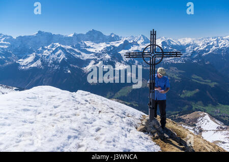 Male hiker debout à côté d'une croix au sommet du Rossstock (2461m) au printemps, écrit son nom dans le livre de sommet. Canton d'Uri, en Suisse. Banque D'Images