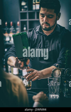 Barman dans tenue formelle servant cocktails derrière comptoir bar. Banque D'Images