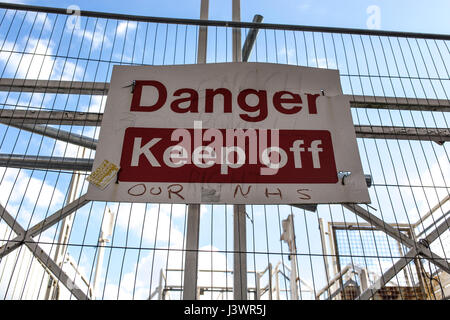 "Attention Garder Off' sign modifié pour dire "attention ne pas notre NHS, attaché au métal forgé et d'un échafaudage. Banque D'Images
