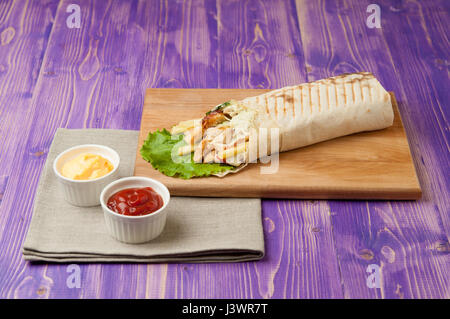 L'arabe shawarma sur planche de bois et deux tasses blanc avec du ketchup et du fromage sur la table en bois Banque D'Images