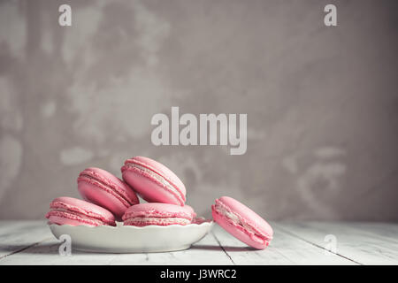 Macarons framboise rose pastel ou macarons sur une plaque sur fond noir en béton Banque D'Images