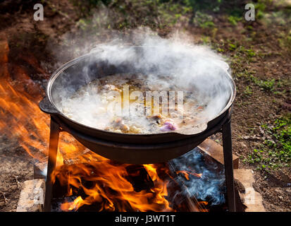 La cuisson pilaf dans un grand chaudron avec une forte la cuisson sur un feu ouvert à l'extérieur sur une journée ensoleillée . Banque D'Images