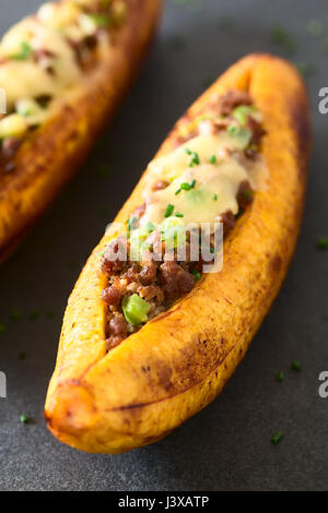 Plantain mûres cuites au four farcies de viande hachée, d'olive, poivron vert et l'oignon, le fromage sur le dessus, parsemer de ciboulette Banque D'Images