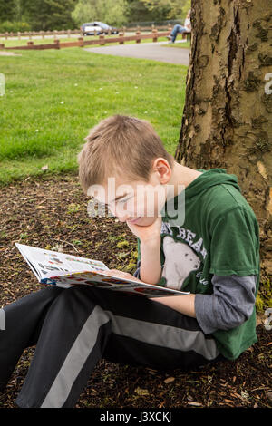 Garçon de neuf ans, la lecture d'un livre à l'ombre d'un arbre en Issaquah, Washington, USA Banque D'Images