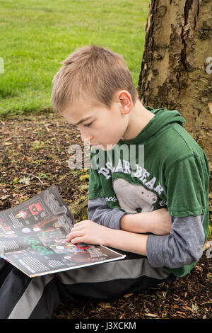 Garçon de neuf ans, la lecture d'un livre à l'ombre d'un arbre en Issaquah, Washington, USA Banque D'Images