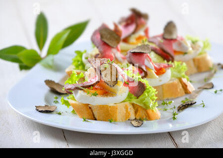 Des canapés avec un rôti de bœuf, truffes d'automne noir, fromage brie française sur une tranche de pain avec un oeuf sur la feuille de salade Banque D'Images