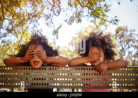 Portrait de deux jeunes sœurs leaning against fence, couvrant les yeux Banque D'Images