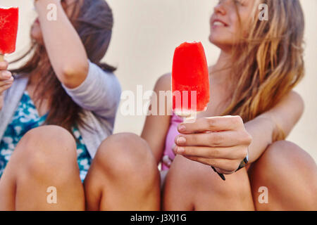 Deux amis, assis à l'extérieur, holding ice lollies Banque D'Images