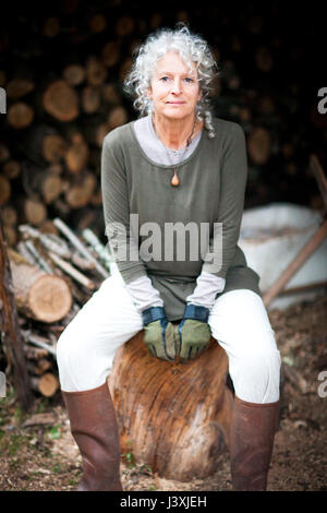 Portrait de femme aux cheveux gris adultes assis sur log in garden Banque D'Images
