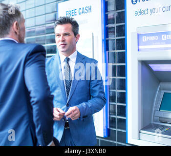 Businessmen talking par cash machine Banque D'Images