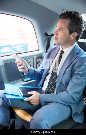 Mature businessman holding smartphone en taxi Banque D'Images