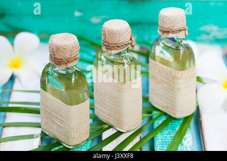 Massage oil set on colorful wooden background with palm leaf and flowers. Copy space Banque D'Images