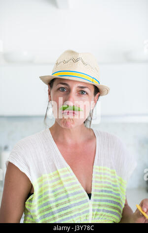 Portrait of mid adult woman in straw hat et pea pod moustache Banque D'Images