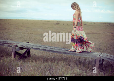 Jeune femme en robe boho marche sur une passerelle en bois en mode paysage Banque D'Images