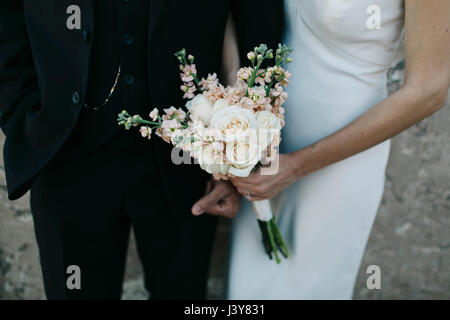 Mariés, bras dessus bras dessous, bride holding bouquet de fleurs, mid section Banque D'Images