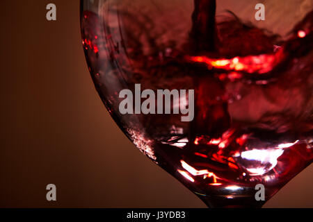 Close-up of red wine vives versé dans le verre et de l'abrégé des éclaboussures contre fond brun. Banque D'Images