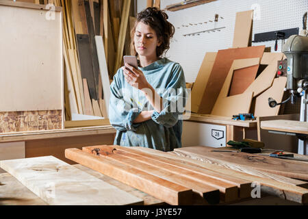 Jeune femme textos dans un atelier bois Banque D'Images
