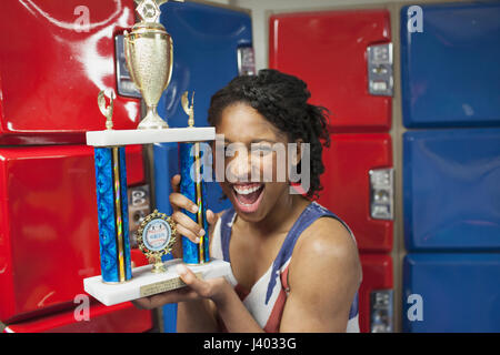 Une jeune femme avec un trophée en avant des casiers rouge et bleu. Banque D'Images