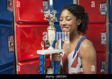 Une jeune femme avec un trophée en avant des casiers rouge et bleu. Banque D'Images