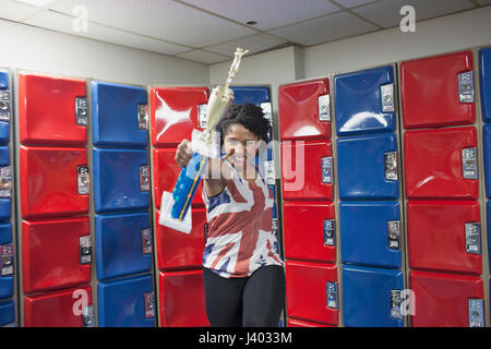 Une jeune femme avec un trophée en avant des casiers rouge et bleu. Banque D'Images