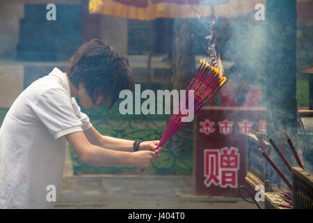 Une jeune femme chinoise s'incline tout en maintenant l'encens à un temple bouddhiste tibétain à Chengde, Chine Banque D'Images