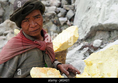 KAWAH IJEN, JAVA, INDONÉSIE - 28 mars : mineurs portent paniers pleins de soufre dans les fumées toxiques des gaz volcaniques au mines de soufre dans le cratère de la loi Banque D'Images