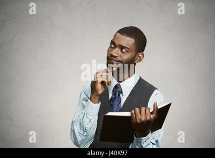 Closeup portrait confus, malheureux homme sérieux holding, reading book, avoir beaucoup de questions, la pensée, l'arrière-plan noir isolé. Visage humain expressi Banque D'Images