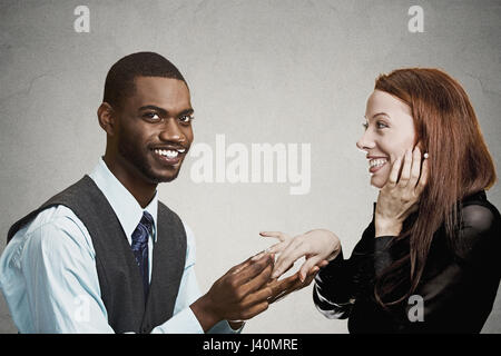 Closeup portrait couple, bel homme heureux propose d'excitée jeune femme gris fond noir isolé. Vacances, amour, relation dati Banque D'Images