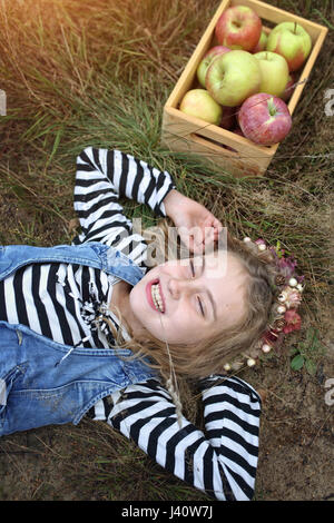 Jeune fille riant se trouve sur l'herbe avec un panier de pommes Banque D'Images