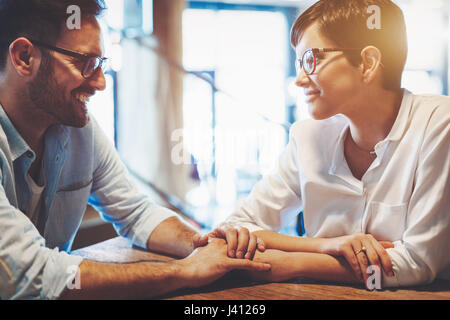 Jeune couple amoureux se tenir la main, se regardant et souriant alors qu'il était assis au café Banque D'Images