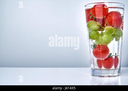 Tomates cerise et les raisins dans un verre à cocktail avec de l'eau dans l'espace de copie. Concept de saine alimentation. Banque D'Images