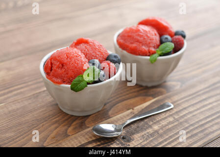 Fruit sorbet à la fraise à la framboise, myrtille et la menthe dans un bol sur fond de bois Banque D'Images