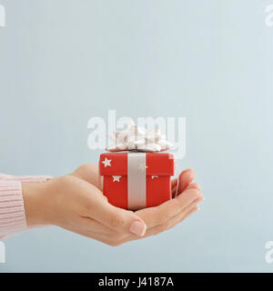 Les mains tenant petit cadeau fort sur fond bleu Banque D'Images