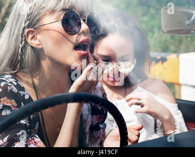 Femme assise dans une voiture en mettant le rouge à lèvres sur des lèvres avec Miroir arrière Banque D'Images