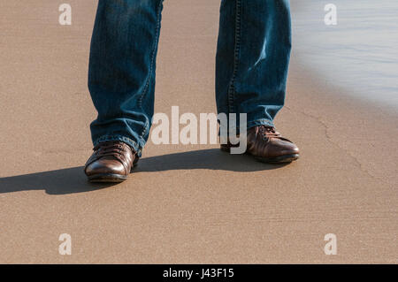 Homme portant chaussures brunes debout sur la plage Banque D'Images