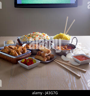 Sélection de la nourriture chinoise et indienne a présenté devant une télévision dans une chambre. Banque D'Images