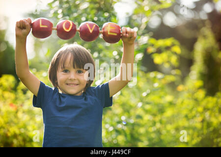 Mignon petit enfant, garçon, tenant un signe d'amour, faite à partir de pommes, lettre grava dans l'apple, souriant joyeusement. bonheur enfance amour concept Banque D'Images