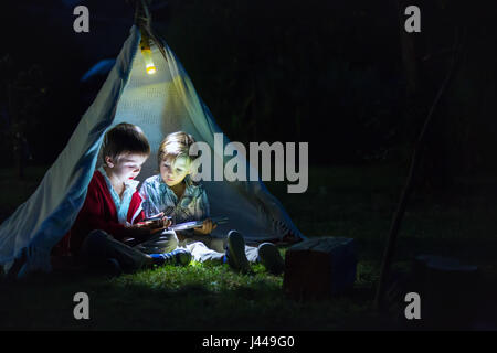 Cute little brothers, jouer sur tablette et téléphone dans la nuit dans la tente, en camping Banque D'Images