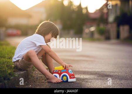 Mignon mon petit enfant, garçon, jouer avec des jouets de voiture sur la rue dans village sur le coucher du soleil, l'été Banque D'Images