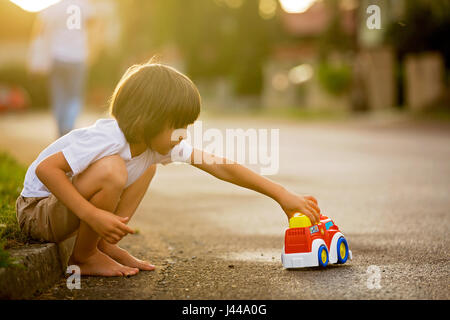 Mignon mon petit enfant, garçon, jouer avec des jouets de voiture sur la rue dans village sur le coucher du soleil, l'été Banque D'Images