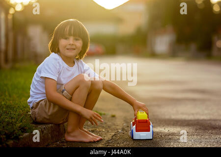 Mignon mon petit enfant, garçon, jouer avec des jouets de voiture sur la rue dans village sur le coucher du soleil, l'été Banque D'Images