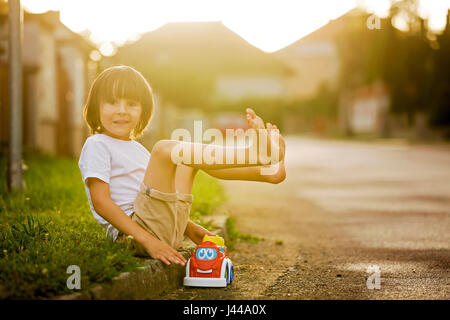 Mignon mon petit enfant, garçon, jouer avec des jouets de voiture sur la rue dans village sur le coucher du soleil, l'été Banque D'Images